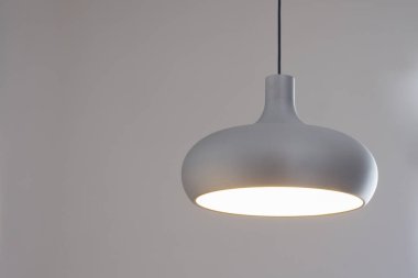 Basit, yarı dairesel şekilli gümüş bir lamba gri bir duvar zemininde asılı duruyor..