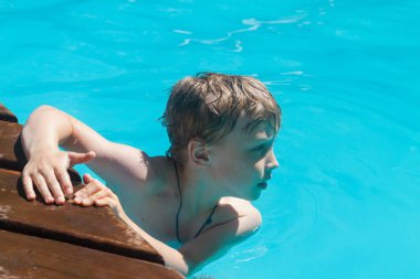 Sarışın beyaz çocuk yazın otelin havuzunda yüzer..