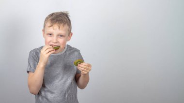 Kafkasyalı bir çocuk yeşil kivi meyvesi yiyor ve gri bir arka planda gülüyor ve gülüyor..