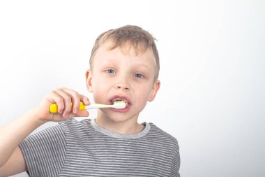 Gri tişörtlü beyaz bir çocuk dişlerini siyah bir kömür diş macunuyla fırçalıyor..