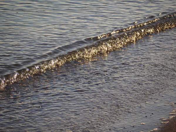 Kumlu bir sahilde yumuşak bir okyanus dalgası. Denizin kıyı dalgası kumlu kıyıya yuvarlanıyor. Enfes bir arka plan. Güneşin altında güzel bir dalga.