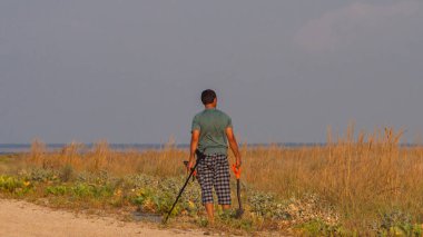 Metal dedektör ve kürekle mücevher ve sikke arayan bir adam. Erkek dikiz aynası. Kopyalamak için yer var. Bir adam metal dedektörü ve küreği olan bir hazine arıyor..