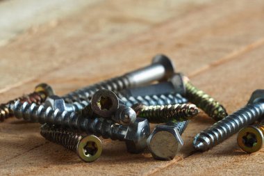 Close-up of metal screws and bolts for wood on a wooden surface with space for text. Accessories for construction and repair.