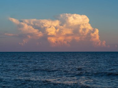 A large cloud over blue sea water with waves. Beautiful cloudy landscape over the sea at sunset.