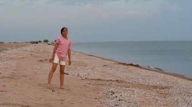 Güzel bir kız deniz sahilinde spor yapıyor. Genç bir kız jimnastik yapıyor ve kumlu bir sahilde sicim üzerinde oturuyor.