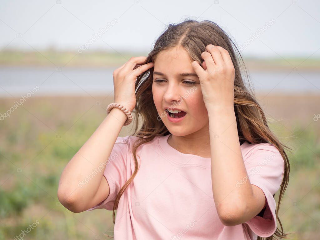 The girl squints. A teenage girl straightens her hair and covers her eyes from the bright light while standing in a spring meadow. Portrait of a sneezing girl.
