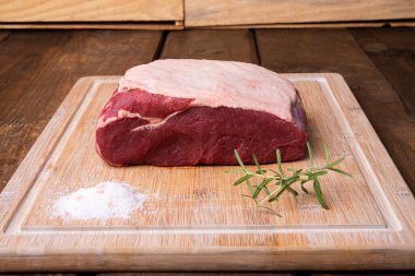 Bir parça sığır filetosu, biberiye ve bambu kesme tahtasında tuz.