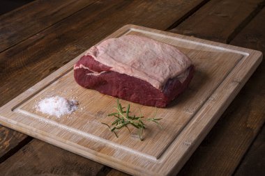 Bir parça sığır filetosu, biberiye ve bambu kesme tahtasında tuz.