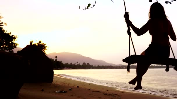 砂のビーチで揺れる女性のシルエットと夕日と山の景色を楽しむ — ストック動画