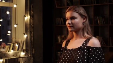 Profil görüşüne göre beyaz bir kadın bir odada duruyor ve röportaj yapıyor.