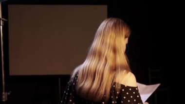 Oyuncu kadrosundaki genç bayan oyuncu metni gözden geçiriyor ve rolünü karanlık odada çalışıyor.