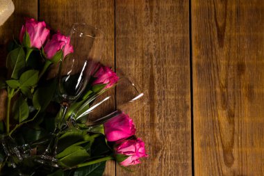 Yukardan çekilmiş iki şeffaf şarap kadehiyle ahşap masada duran güllerin yakın çekim görüntüleri.