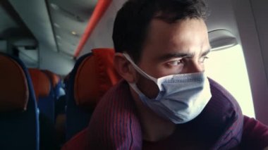 Tıbbi maskeli beyaz sakallı bir adamın portresi uçağın içinde oturup etrafa bakınıyor.