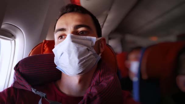 Retrato de un joven pasajero caucásico sentado en el avión usando máscara facial y sintiéndose cansado — Vídeos de Stock