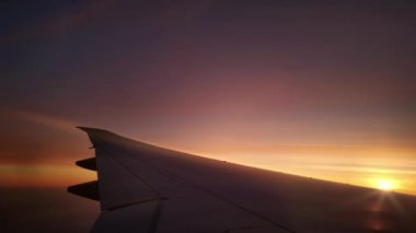 Uçak kanadı pembe günbatımı gökyüzünde uçuyor. Pencereden çekilen bulutların üzerinde.
