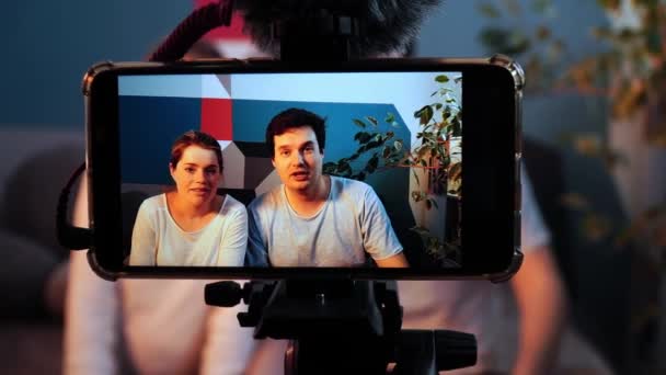 Close-up de smartphone em pé em uma sessão de fotos e filmando uma entrevista de homem e mulher jovem — Vídeo de Stock