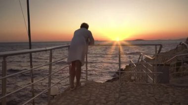 Gözlem noktasında duran ve parmaklıklara yaslanan adam dalgalı denizde günbatımının tadını çıkarıyor.