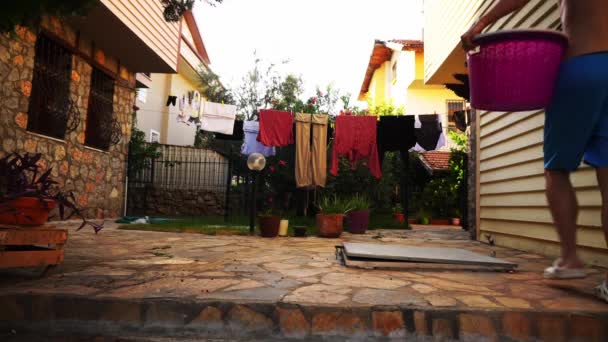 Man in blue shorts is taking off clothes from the rope which were drying after laundry outdoors — Stock Video