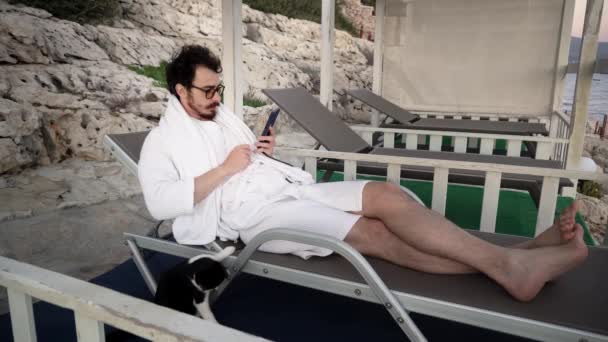 Чоловік відпочиває на сонячному ліжку, коли хтось телефонує йому на смартфон і каже погані новини — стокове відео