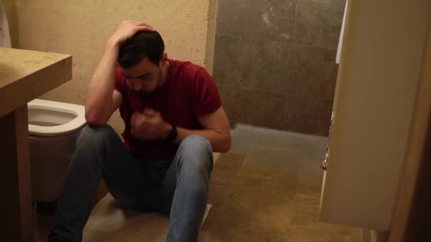 Young sick guy is sitting on the floor of bathroom next to toilet and holding his belly — Vídeo de Stock