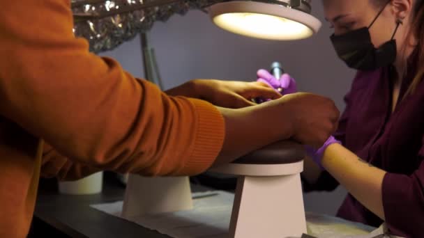 Woman hand doctor in a protective mask gives a manicure to a black man in a beauty salon — Stockvideo