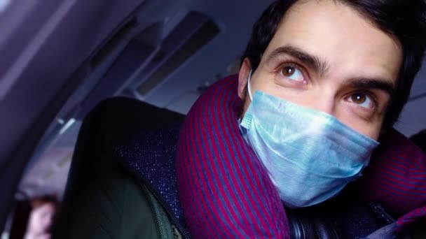 의료용 마스크를 쓴 쾌활하게 주의 깊은 사람 이 비행기 안에 앉아 창밖을 내다보고 있습니다 — 비디오