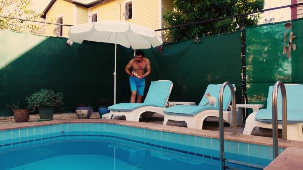 Man is coming to swimming pool with sunbeds and putting sun lotion on his body before sunbathing — 图库视频影像