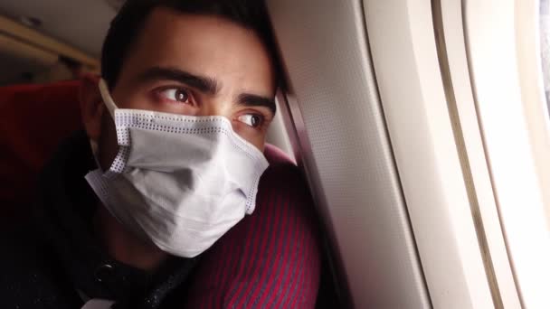 Tired man in a medical face protective mask sits on an airplane and looks out the window — Vídeos de Stock