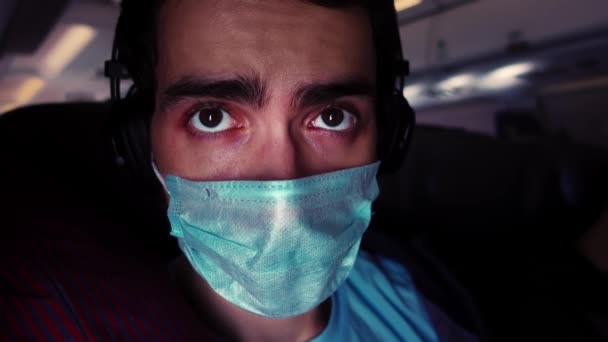 Ung kaukasisk man tittar genom fönstret under en flygning på flygplan bär medicinsk mask — Stockvideo