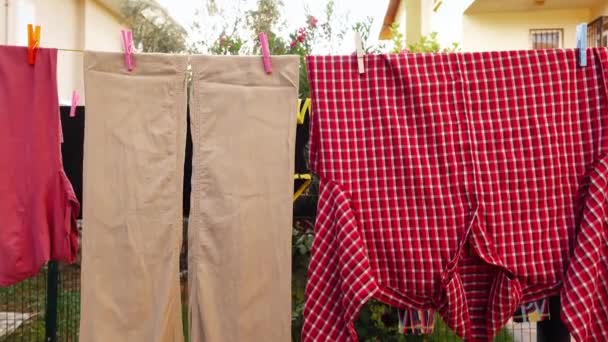 Pantalon beige et chemise à carreaux rouges sont suspendus sur la corde à linge attachée par des épingles — Video