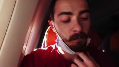 Genç sakallı adamın portresi su içmek için maskesini çıkarıyor ve güvertede otururken takıyor.