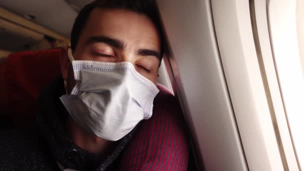Retrato de un joven caucásico con máscara facial sentado en el avión y mirando por la ventana — Vídeos de Stock