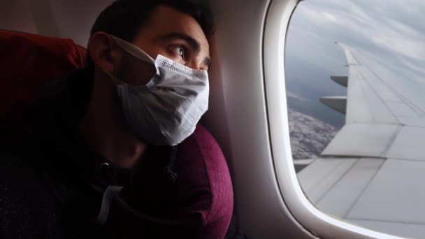 Pasajero cansado está mirando a través de la ventana de un avión donde hay ala y ciudad — Vídeos de Stock