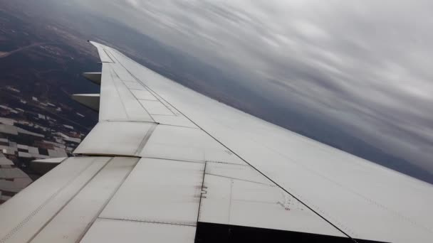 Vista del ala del avión volando sobre la ciudad con azoteas y girando hacia tierra — Vídeos de Stock