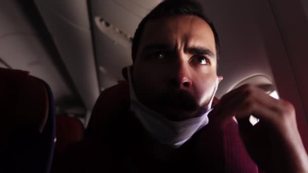 Närbild av kaukasisk manlig passagerare i flygplanet drar ner mask på hakan — Stockvideo