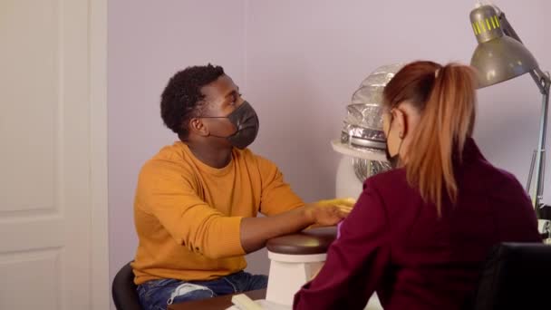 Zwarte jongeman zit in spa salon en zet zijn handen voor de meester om manicure te maken — Stockvideo