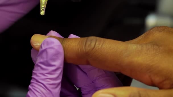 Maniküre tropft Öl aus Pipette auf Fingernagel von schwarzem Mann und beginnt es mit Schwamm zu polieren — Stockvideo