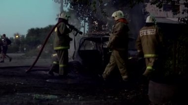 İtfaiyeciler yanan bir arabanın üzerine su hortumundan su döker.