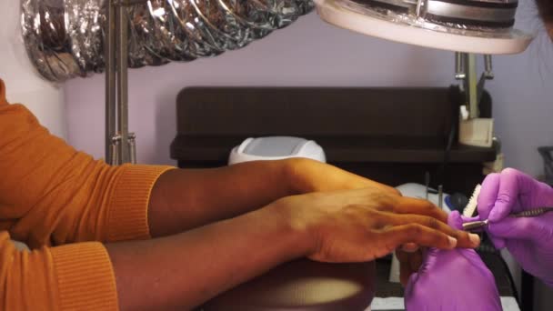 Vrouwelijke meester in beschermende handschoenen maakt manicure aan zwarte man in een salon in close-up — Stockvideo