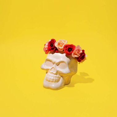 Üstünde insan kafatası ve çiçek çelengi var. Parlak sarı arka plana karşı yaratıcı korku düzeni. Korkunç komik bir stil..