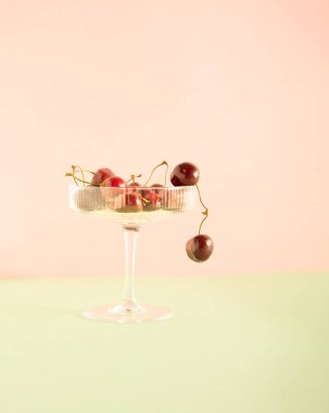 Art Deco kristal moda şampanya bardağı ve taze kiraz meyvesi, yaratıcı bahar ya da yaz esinlenilmiş düzenleme pastel pembe arka plana karşı. Güzel doğa ve sağlıklı ferahlatıcı fikirler. 