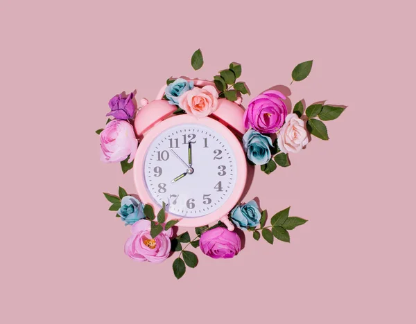 Pink retro alarm clock, creatively decorated with colorful flowers. Spring floral layout. Good morning idea. 