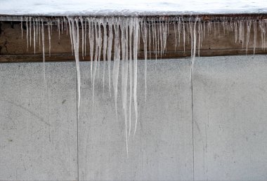 melting icicles on the eaves of the roof of the house in winter. a row of large transparent icicles.