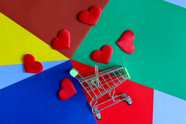 Kırmızı sevgililer günü kalpleri çok renkli bir geometrik arka plan ve alışveriş arabasına saçılmış. — Stok fotoğraf