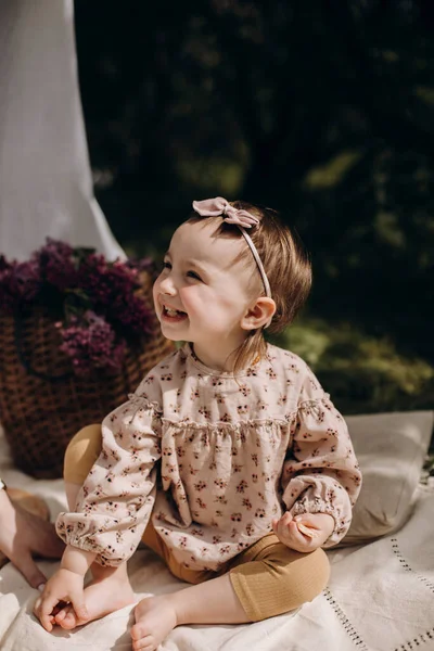 快乐的女婴大声笑着 朝旁边看去 快乐的小女孩坐在野餐毛毯上 头戴蝴蝶结的女婴 — 图库照片