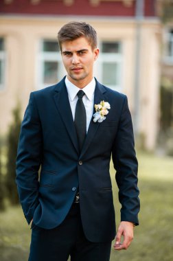 Takım elbiseli yakışıklı damat ve dışarıda poz veren beyaz gömlek.