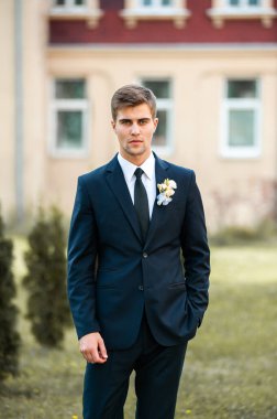 Dışarıda poz veren takım elbiseli yakışıklı bir damat.