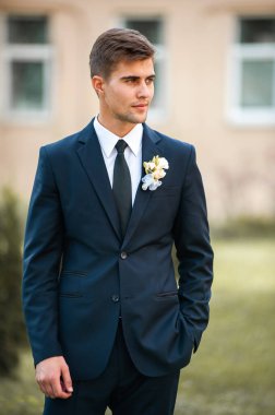 Dışarıda poz veren takım elbiseli yakışıklı bir damat.