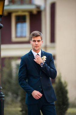 Takım elbiseli yakışıklı damat, mavi ceketli beyaz gömlek ve düğün gününde kravat.