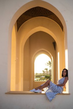 Beyaz elbiseli, arka planda mavi gömlekli güzel bir kadın.